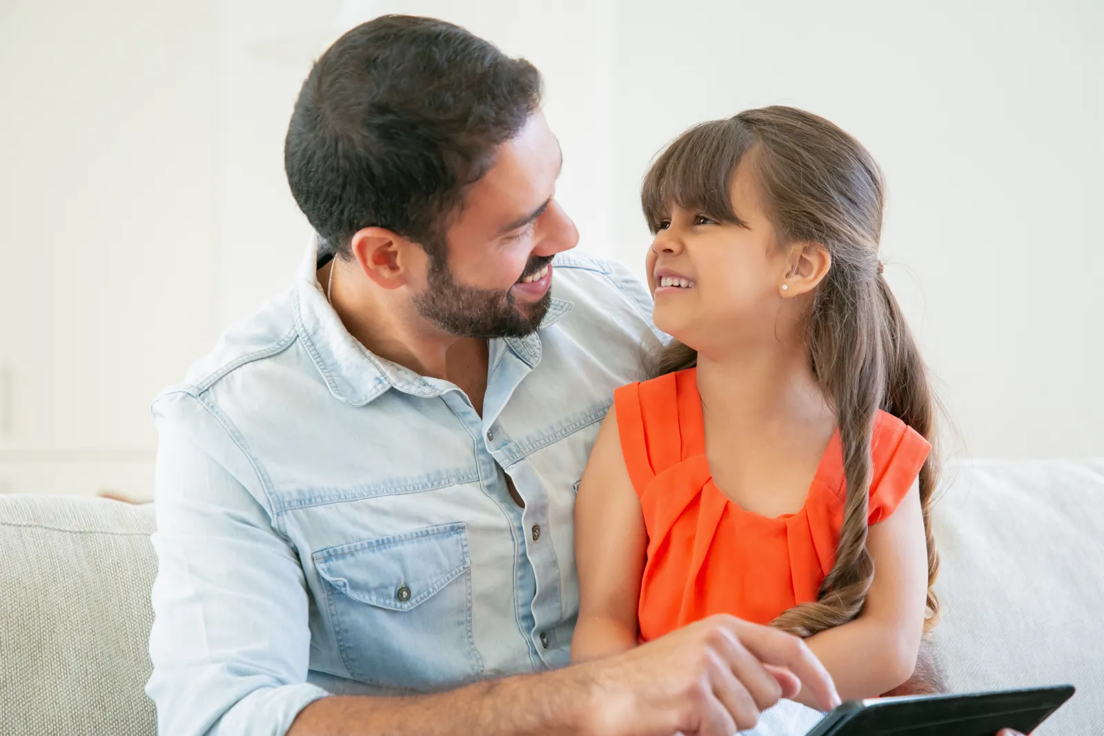 Un père et sa fille se sourient devant une tablette