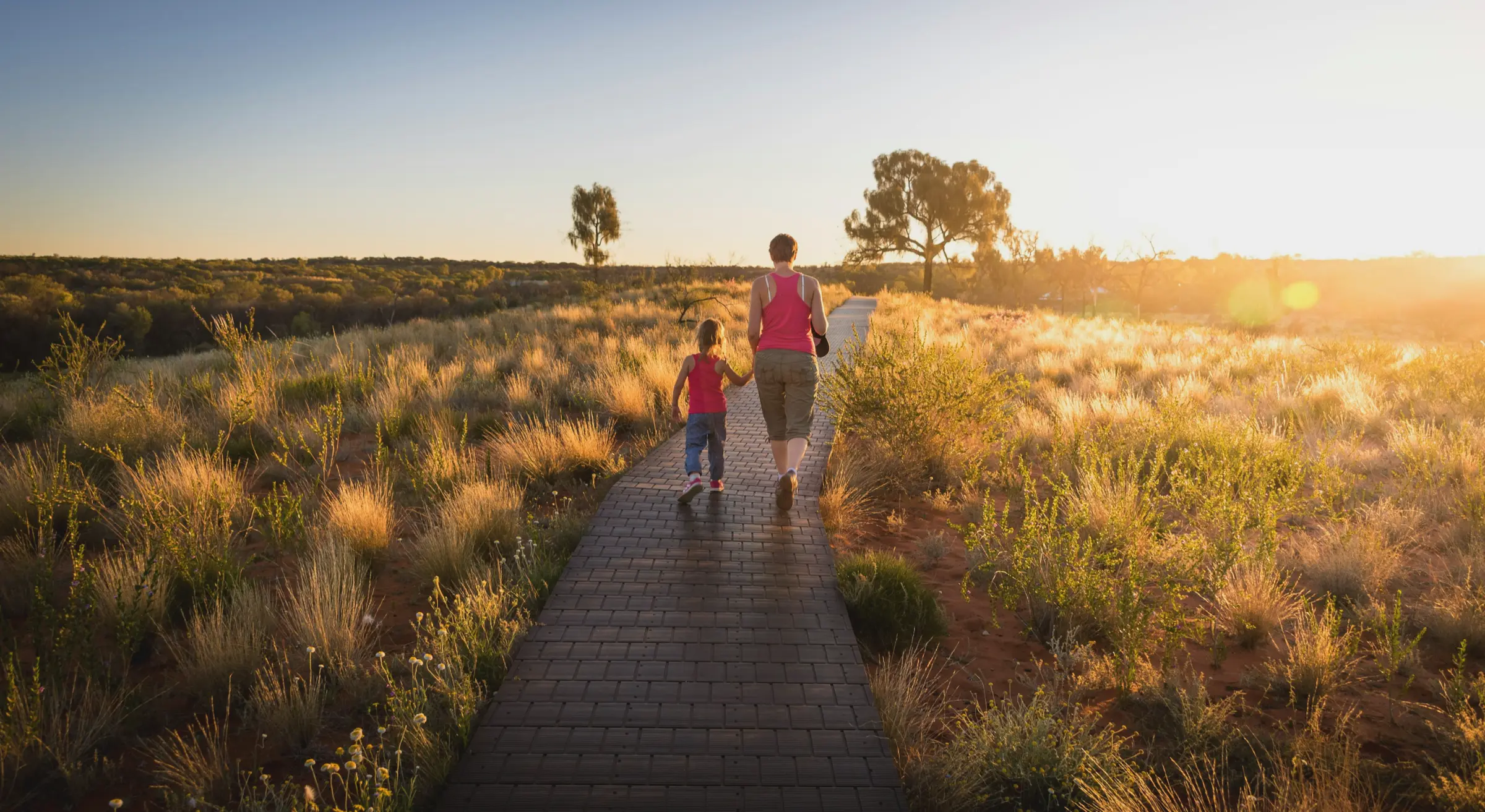 Un parent et son enfant marchent sur un sentier au coucher du soleil