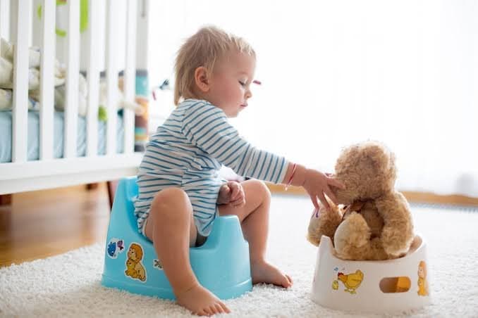 Un jeune enfant sur un pot et joue avec sa peluche qui est sur un pot