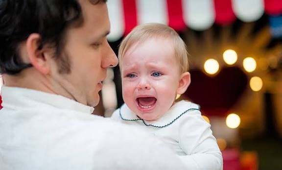 Bébé en pleurs dans les bras d’un adulte, illustrant l’angoisse de séparation chez le jeune enfant
